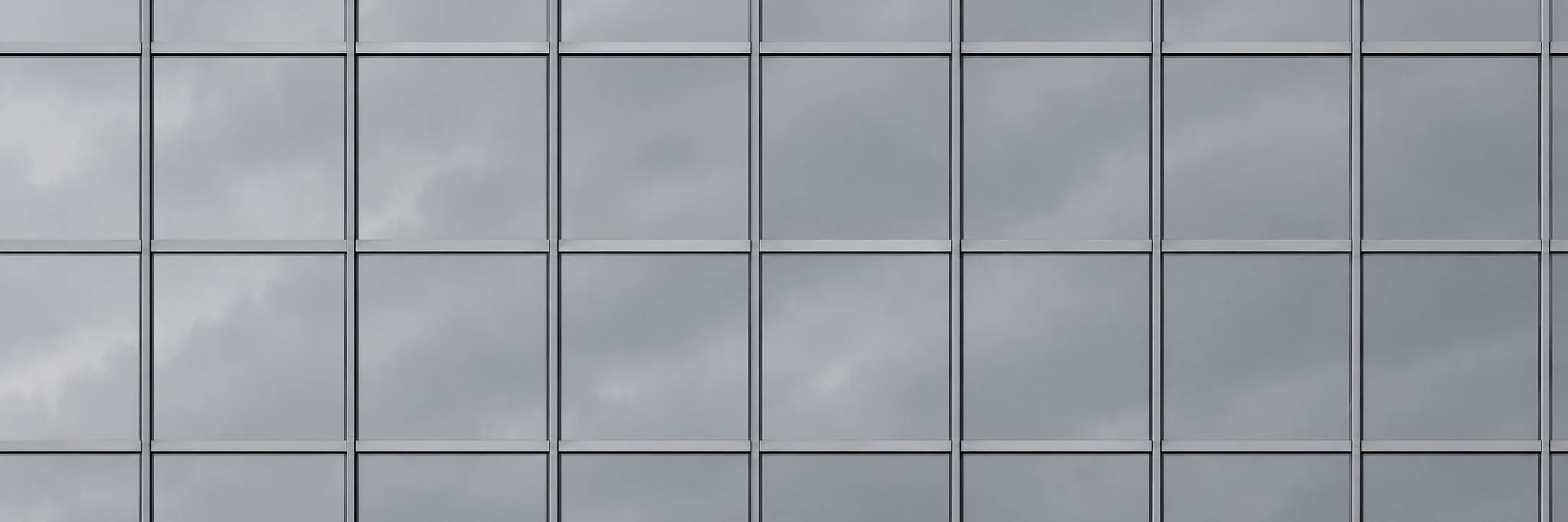 Fachada espelhada de edifício corporativo, com a grade de vidros refletindo o céu nublado.